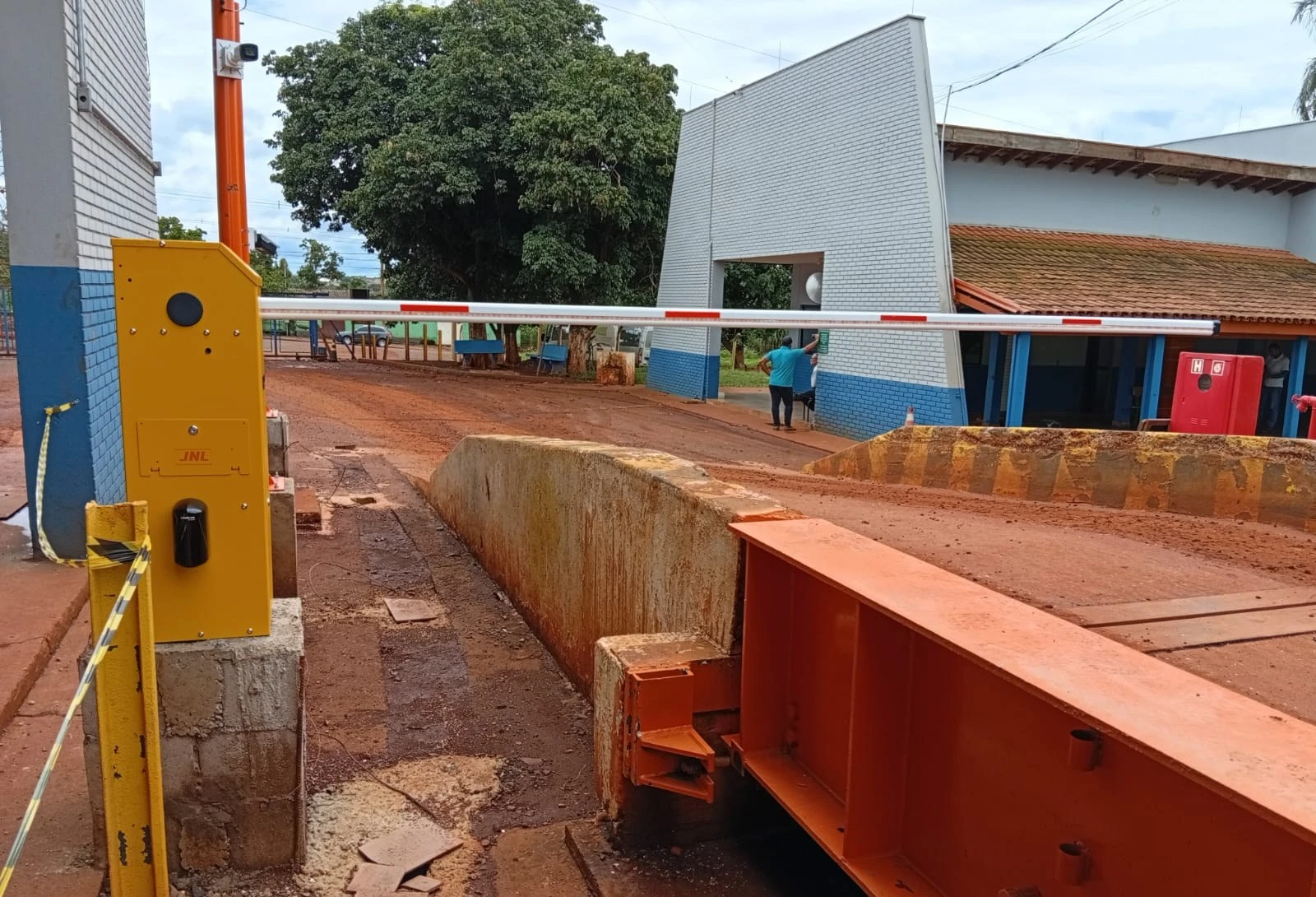 Cancela amarela e totem na cabeceira de uma balança rodoviária metálica, em obra da JNL