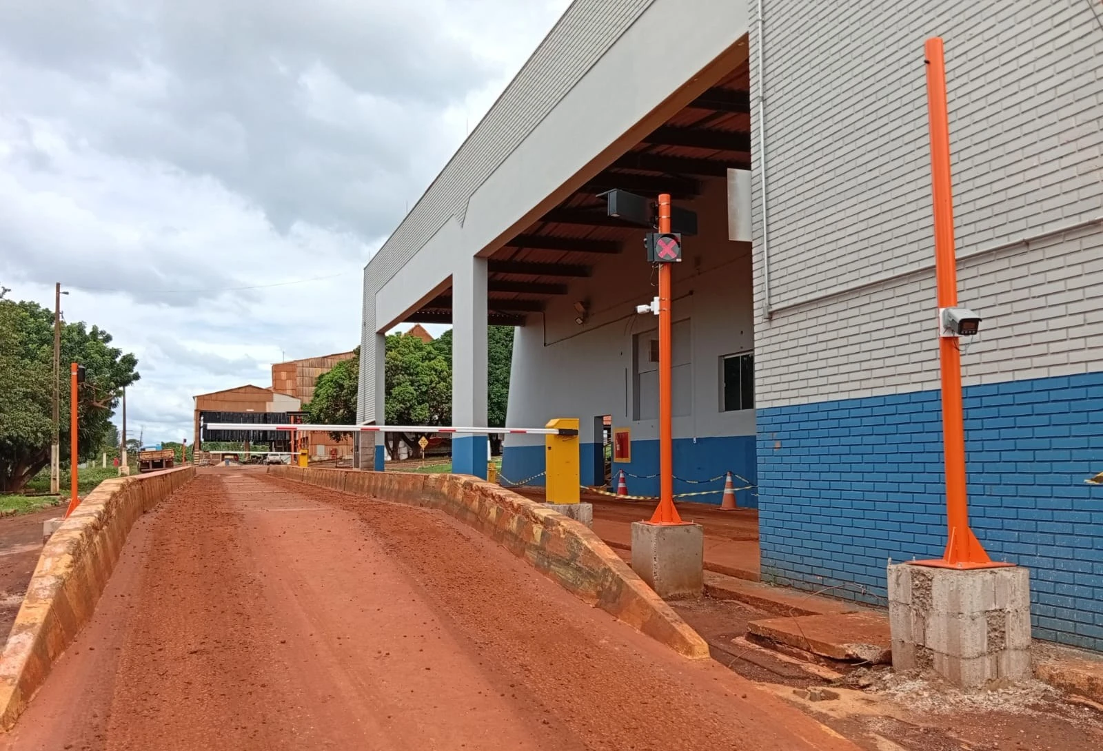 Postes laranja com câmera, semáforo e display remoto ao lado da pista de pesagem, em obra da JNL